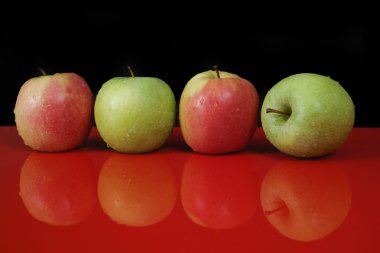 Fresh green and pink apples on red table top and black backgroun