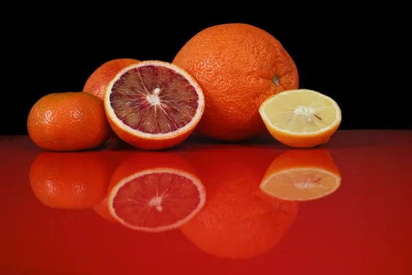 Various fresh citrus fruits on red table top with reflection and — Stock Photo, Image