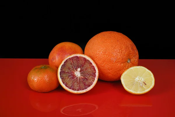 Various fresh citrus fruits on red table top  and black backgrou — Stock fotografie