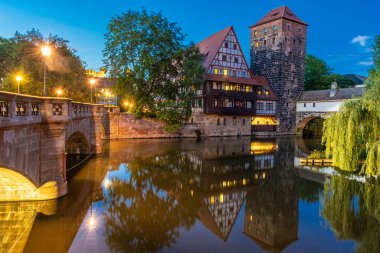 Nuremberg, Franconia, Almanya 'da Pegnitz nehrinin kıyısındaki yarı keresteli eski evlerin renkli ve pitoresk bir manzarası gece aydınlandı.