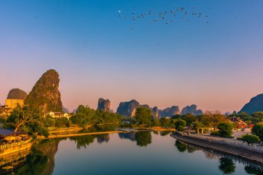 Gün batımında Çin 'de Yangshuo' da Li Nehri üzerinde uçan kuş sürüsü.
