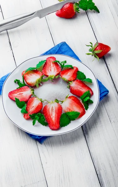 Slice of strawberry with leaf of mint  on white plate and two be