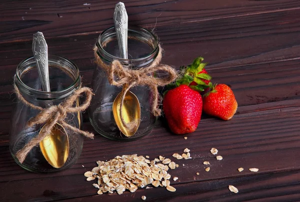 Dois jarros vazios com colher de bronze flocos de aveia espalhados e morango — Fotografia de Stock