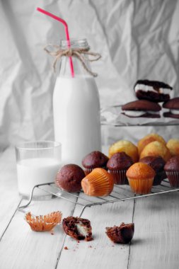 beyaz ahşap masa dağınık çikolata ve basit mini kekler. Seçici odak. Biten (kırık) ilk planda birçok kekler ve ikinci planda tübüle süt şişesi.