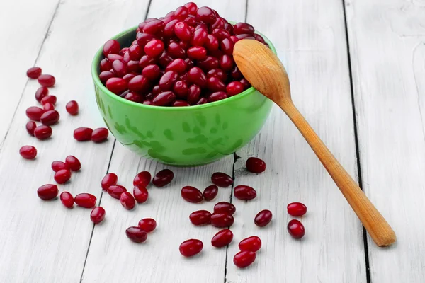 Frische reife Kornelbeeren in grünem Teller und verstreute Beeren mit Holzlöffel auf hölzernem Hintergrund. Selektiver Fokus — Stockfoto