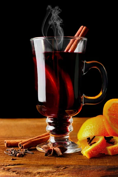 Hot mulled wine glass with spices (canmon sticks, star anise, dried lemon) on a wooden table.Vertical shot.Cutted orange.Selective focus.Black background — Stock Photo, Image