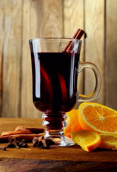 Hot mulled wine glasswith spices (canmon sticks, star anise, dried lemon) on a wooden table.Vertical shot.Cutted orange.Selective focus.Wooden background — Stock Photo, Image