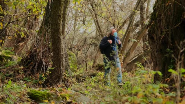 森の中の森の中を長い髪をした防護マスクの孤独な男がひとりで歩いている コロナウイルスの脅威による隔離 Covid 19ウイルス — ストック動画