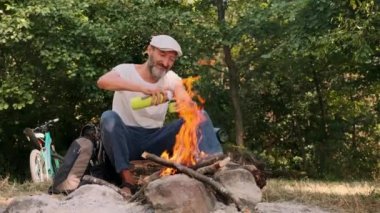 Açık havada, ateşin yanında sakallı bir adam termostan çay ve kahve döküyor. Yakın plan. Yaz ormanında kamp yapmak. Doğada piknik.