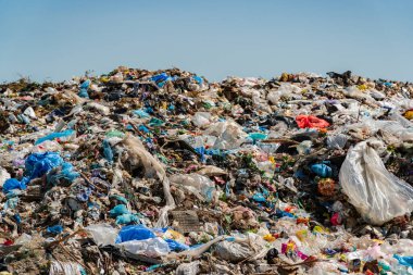 A sprawling landfill site overflowing with colorful plastic and other waste, contributing to pollution and ecological harm.