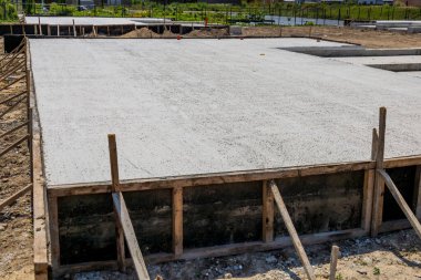 Workers prepare a cement slab for the foundation of a house in a residential construction site during a bright day.
