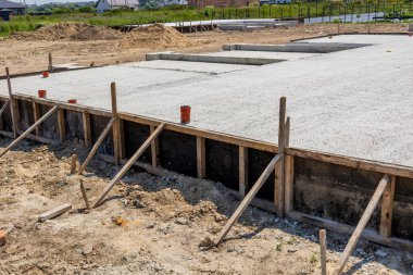 Construction workers pour cement to create a solid foundation for new houses on a development site under clear blue skies.