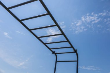 A horizontal bar stands against a clear blue sky in a park, inviting people to engage in fitness training and active exercise routines.