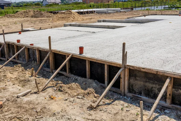 Construction workers pour cement to create a solid foundation for new houses on a development site under clear blue skies.