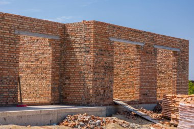Workers are constructing brick walls for a new house in a residential area under clear blue skies, showcasing the building process.