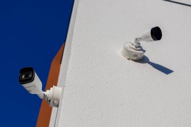 Beyaz bir duvara iki güvenlik kamerası yerleştiriliyor, temiz bir gökyüzü ortamında gözetleme ve koruma sağlıyor..