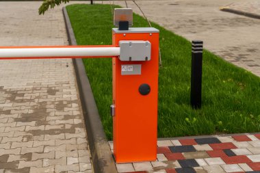 Parlak turuncu bir park engeli kaldırımın yanında duruyor. Çevresinde yeşil çimenler olan temiz ve düzenli bir otoparka erişimi kontrol ediyor..