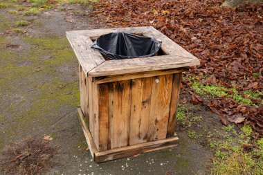 Ahşap bir çöp tenekesi, renkli yapraklarla çevrili bir patikada duruyor. Parkta sonbaharın güzelliğini gözler önüne seriyor..