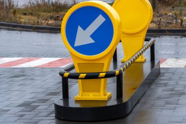 Yuvarlak mavi trafik levhası, aşağı doğru beyaz bir ok ile şehir merkezindeki bir yolun yanındaki sarı bir üste duruyor..