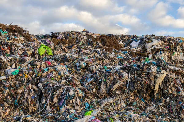 Büyük bir çöp sahasında güpegündüz bulutlu bir gökyüzünün altında plastik ve kumaş atıkları da dahil olmak üzere yığınla çöp sergileniyor..