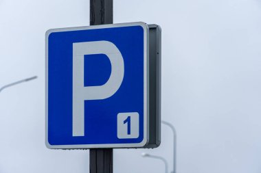 Canlı bir şehirde mavi bir park levhası, sürücüleri gri gökyüzünün altındaki boş noktalara yönlendiriyor..