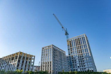 Yeni binalar parlak mavi gökyüzüne karşı yükseliyor, vinçler inşaat alanında özenle çalışarak kentsel gelişimi sergiliyor..