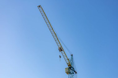 Uzun bir vinç canlı mavi gökyüzüne karşı gururla duruyor, hareketli bir şehirde gelişmeyi ve altyapı gelişimini simgeliyor..