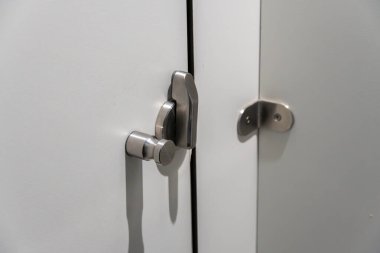 Zarafetle dolu, aydınlık, minimalist bir alanda çağdaş bir dolap kapısını koruyan parlak metal bir donanım..