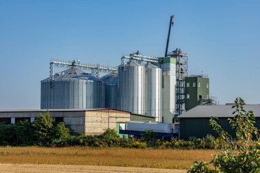 Yüksek silolar açık mavi gökyüzüne karşı yükselirken, yakınlardaki makineler tarım endüstrisini kolaylaştırırken, hasat için hazır altın tanelerini depoluyorlar..