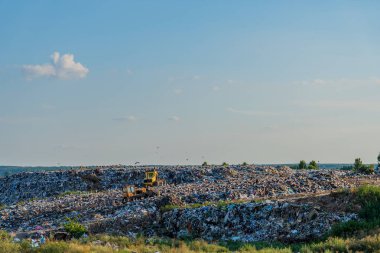 Açık mavi gökyüzü altında muazzam bir çöp yığını yayılıyor, atık yönetimi ve ekolojik etkisinin giderek artan zorluğunu ima eden çöp yığınları..