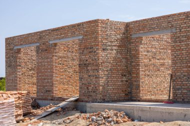Becerikli inşaatçılar sağlam bir duvar için tuğla döşüyorlar. Güneşli bir şantiyede işçilikle modern tasarımı harmanlıyorlar..