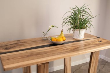 Tahta bir masa, bir kase meyve ve bir saksıyı gündüz vakti ev ortamında tutar..