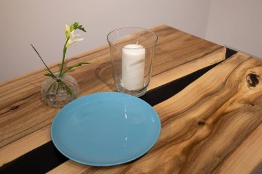 Basit bir masanın mavi bir tabağı, cam bir mum tutacağı ve çiçekli küçük bir vazosu vardır. Ayarlar bir evde gündelik dekorasyonu gösterir.