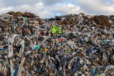 Ufuk boyunca uzanan geniş bir çöp yığını bulutlu bir gökyüzünün altında parlak plastikler ve organik kalıntılar sergiliyor..
