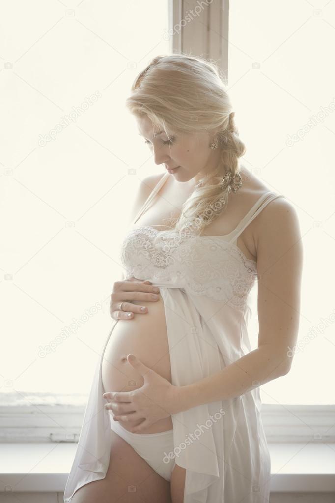 Beautiful pregnant blond woman in a bright room