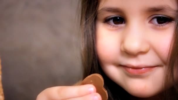 Little Girl Face Close Up With Long Hairs está mirando en la cámara y sonriendo. Pequeña hermosa chica degustar chocolates con gusto . — Vídeo de stock