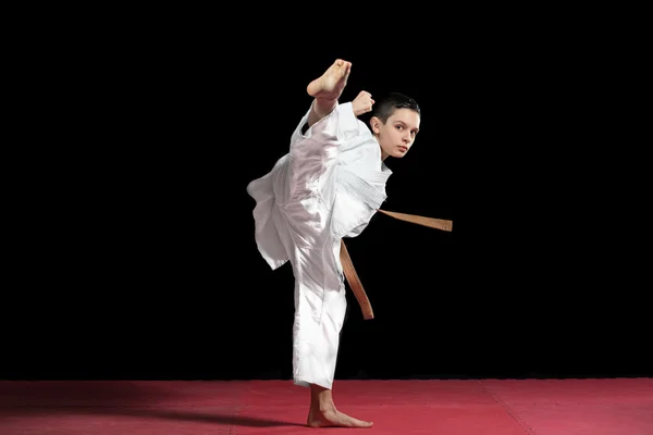 Парень-каратист в белом кимоно сражается изолированно на черном фоне — стоковое фото