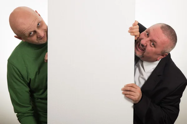 Dois homens elegantes sorrindo depois de um painel vazio no fundo branco — Fotografia de Stock