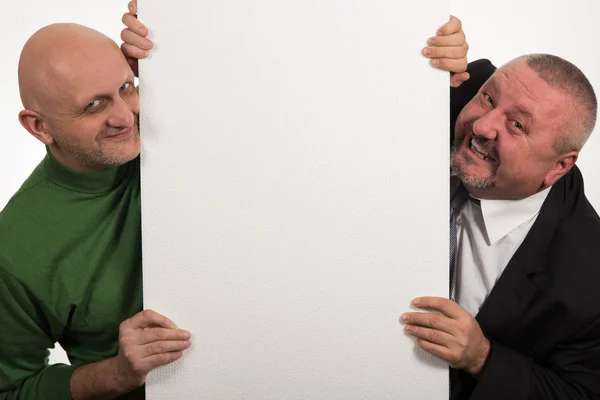 Dois homens elegantes sorrindo depois de um painel vazio no fundo branco — Fotografia de Stock