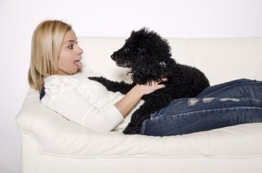 Siyah bir fino köpeği ile beyaz kanepede yatan kadın.