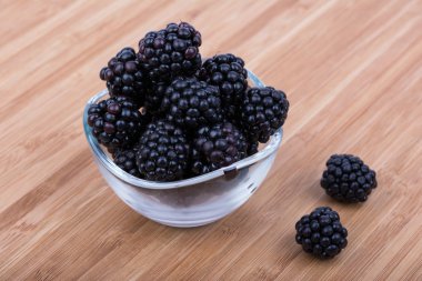 Ahşap arka plan üzerinde bir kasede olgun böğürtlen