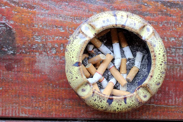 Cigarett, rökning, luftföroreningar, rökning, fara. Askfat med stub på bordet med ovanifrån — Stockfoto