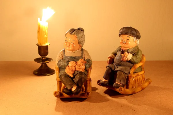 Ακόμα φωτογραφία ζωή με υπέροχο ζευγάρι ανώτερος κούκλα χωροθέτηση λικνίζοντας καρέκλα μπαμπού με το φως των κεριών στο σκοτάδι σε φόντο ξύλου. — Φωτογραφία Αρχείου