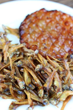 Kızarmış dev yayın balığı ve kızartılmış küçük balıklar (Minnow) geleneksel Tayland tarifleri kırsal ahşap arka planda beyaz tabakta. Tayland 'da popüler, Tayland' ın önemli ihracat ürünü.