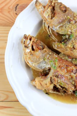 Tayland Devi gourami balığı ve sarımsak. Çam ağacından masada, beyaz tabakta kızartılmış tatlı ve baharatlı sos. Tatlı biberli kızarmış balık. Baharatlı soslu Tayland yemeği. Tayland tarzı yemek..