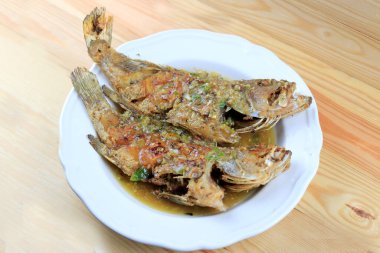 Tayland Devi gourami balığı ve sarımsak. Çam ağacından masada, beyaz tabakta kızartılmış tatlı ve baharatlı sos. Tatlı biberli kızarmış balık. Baharatlı soslu Tayland yemeği. Tayland tarzı yemek..