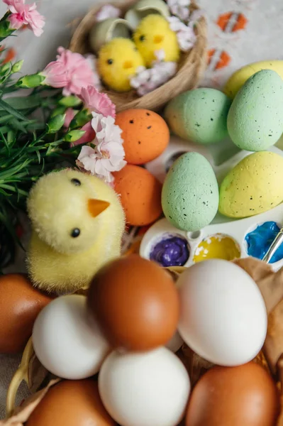 Canlı bir Paskalya yaratıcı düzeneği, doğal ve renkli boyanmış yumurtalar, parlak boyalı bir sanat paleti, ve sevimli sarı piliçler. Pembe karanfiller ve küçük bir yuva bu sanatsal tatil kompozisyonuna şenlikli bir bahar dokunuşu ekler. Üst görünüm.