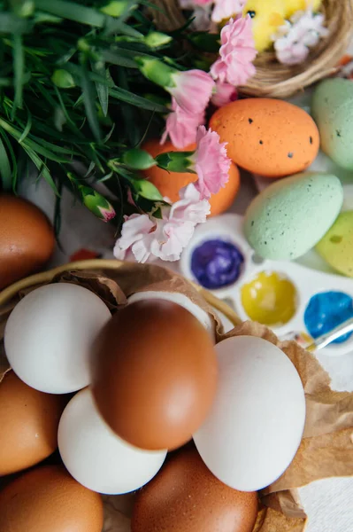 Canlı bir Paskalya yaratıcı düzeneği, doğal ve renkli boyanmış yumurtalar, parlak boyalı bir sanat paleti, ve sevimli sarı piliçler. Pembe karanfiller ve küçük bir yuva bu sanatsal tatil kompozisyonuna şenlikli bir bahar dokunuşu ekler. Üst görünüm.