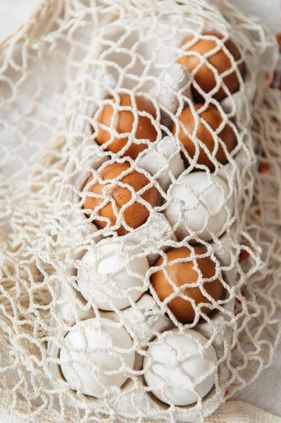 Karton bir karton kutunun içinde organik kahverengi ve beyaz yumurtaların olduğu, sürdürülebilir pamuk bir çantaya sarılı sıcak bir Paskalya. Onun yanında, küçük bir kuş yuvası iki sarı tüylü civciv ve kırsal bir keten arka planda narin çiçekler barındırır. Bahar.