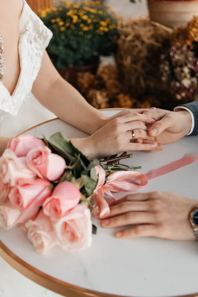 Gelin ve damadın ellerini gösteren güzel bir düğün serisi. Altın alyansların yakın çekimleri, yeni evlilerin el ele tutuşmaları ve bir buket pembe güller de dahil. Düğün töreninin romantik atmosferi, mücevherlere, çiçeklere odaklan,